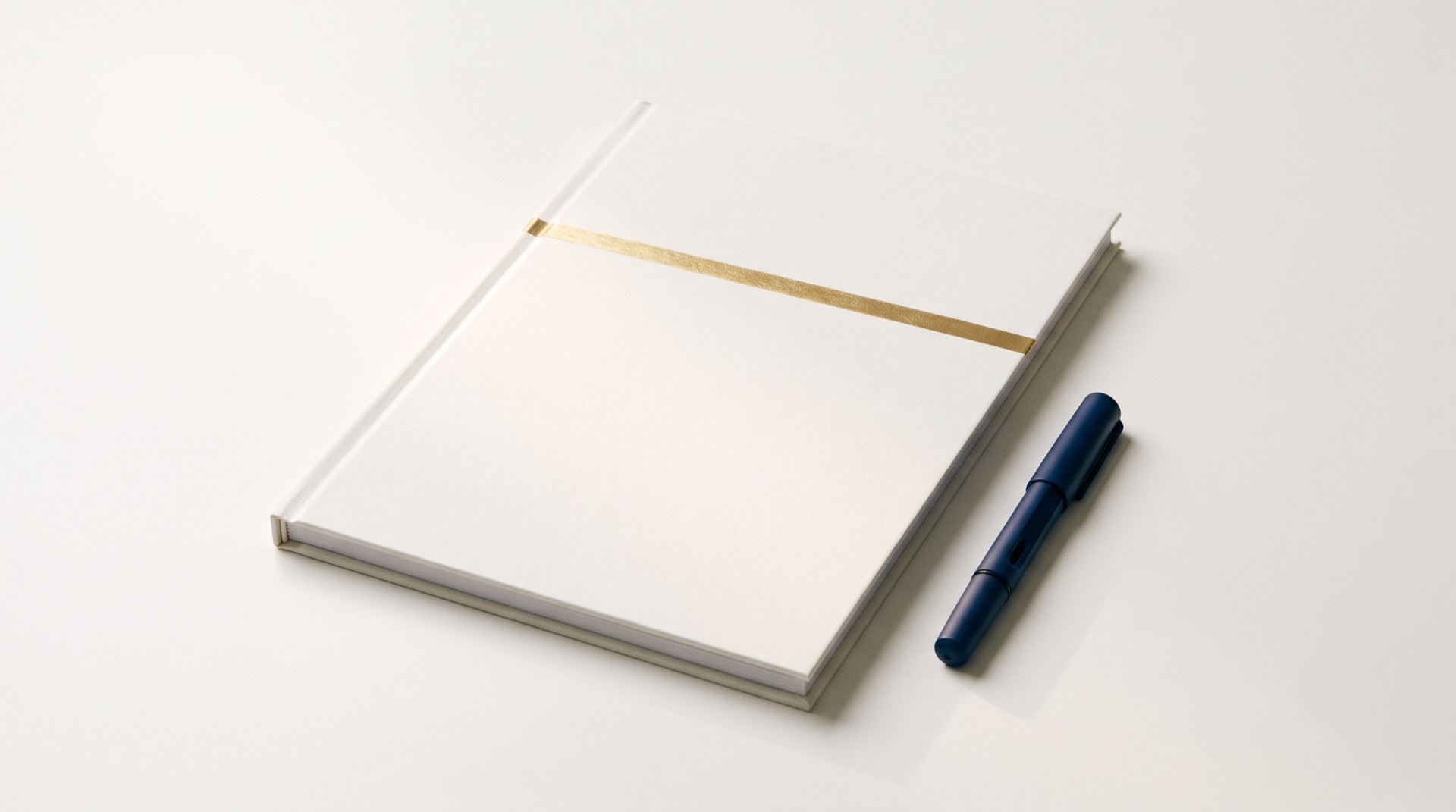 A closed bound report with a thin gold band on its cover, lying on a clean white desk beside a navy fountain pen.